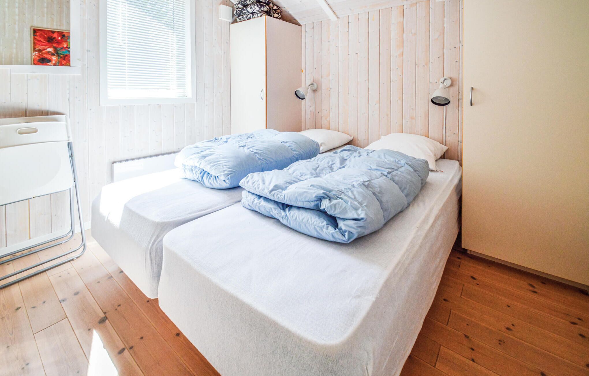 A single bed with a white mattress and blue bedding in a room with wooden walls and a window.