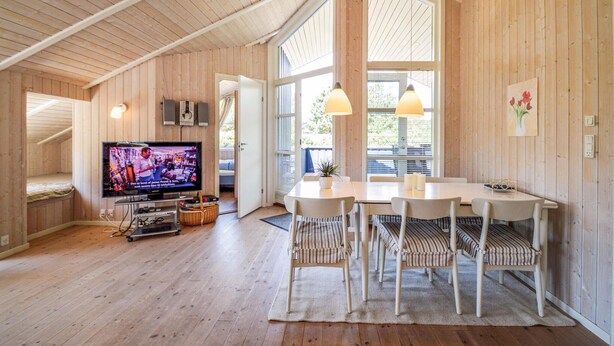 Un intérieur chaleureux en bois, avec un coin repas, un téléviseur et une grande fenêtre.