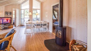 Un salon chaleureux avec un décor intérieur en bois, une cheminée, un coin repas avec des meubles blancs et un téléviseur.