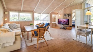 Un salon chaleureux avec un plafond en bois, un canapé, une table à manger, des chaises en osier et un téléviseur.