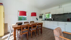 A modern kitchen with white cabinets, a wooden dining table, and red pendant lights.