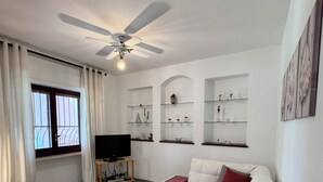 Ein Wohnzimmer mit einem weißen Sofa, einem TV-Schrank und Regalen mit Dekoration.