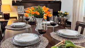 Ein Esstisch gedeckt mit Tellern, Gläsern und einer Blumenschale mit orangefarbenen Tulpen.