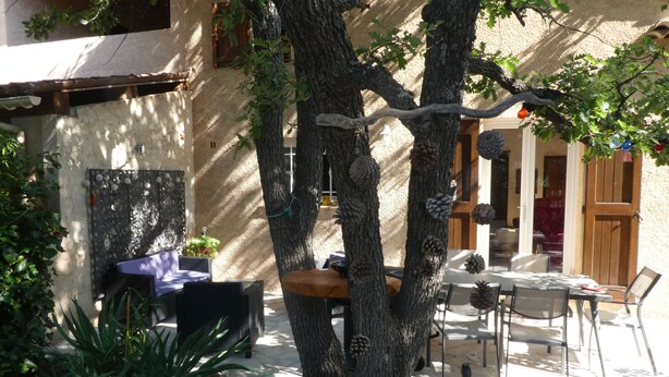 An outdoor patio with a dining table and chairs, surrounded by a stone wall and a tree with pinecones. - PROVENCE: HOUSE IN LES SALLES/VERDON, 400 M FROM LAC DE SAINTE-CROIX, GORGES DE L'OUEST (Les Salles-Sur-Verdon)