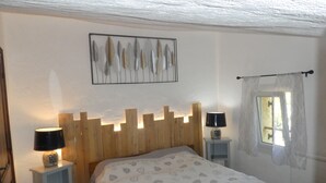 A bedroom with a wooden headboard, a bed with a patterned bedspread, bedside lamps, a wall-mounted artwork, and a window with curtains. - PROVENCE: HOUSE IN LES SALLES/VERDON, 400 M FROM LAC DE SAINTE-CROIX, GORGES DE L'OUEST (Les Salles-Sur-Verdon)