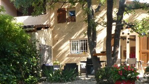 A courtyard with a stone pathway, potted plants, and a building with a tiled roof. - PROVENCE: HOUSE IN LES SALLES/VERDON, 400 M FROM LAC DE SAINTE-CROIX, GORGES DE L'OUEST (Les Salles-Sur-Verdon)
