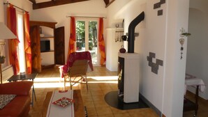 A cozy living room with a fireplace, wooden beams, a dining area with a table, and a view through a glass door. - PROVENCE: HOUSE IN LES SALLES/VERDON, 400 M FROM LAC DE SAINTE-CROIX, GORGES DE L'OUEST (Les Salles-Sur-Verdon)