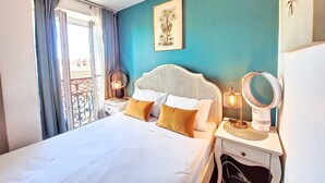 Ein Schlafzimmer mit einem Bett, zwei Nachttischen mit Lampen, einem Wandspiegel und einem Fenster mit Vorhängen.