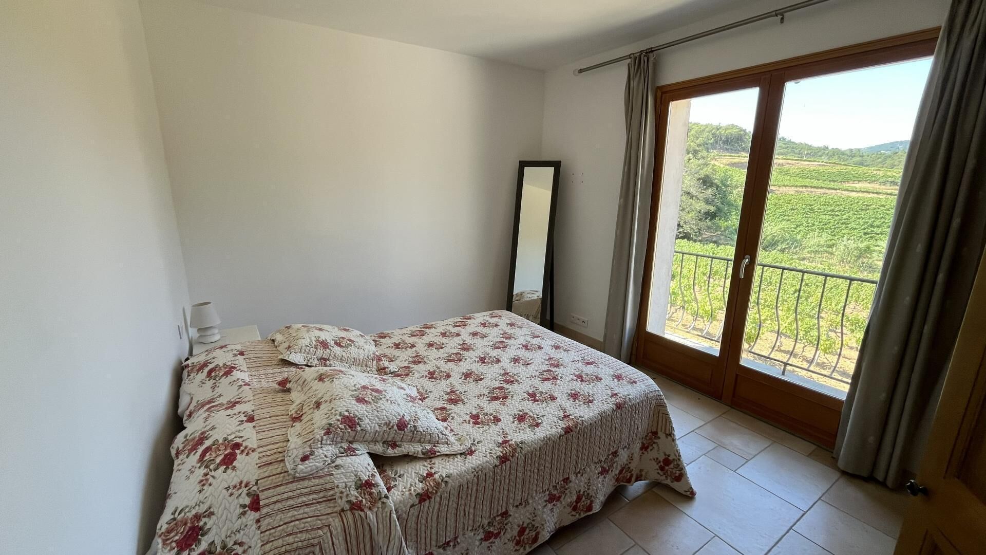 Une chambre à coucher avec un lit, un miroir et un balcon donnant sur un espace verdoyant.