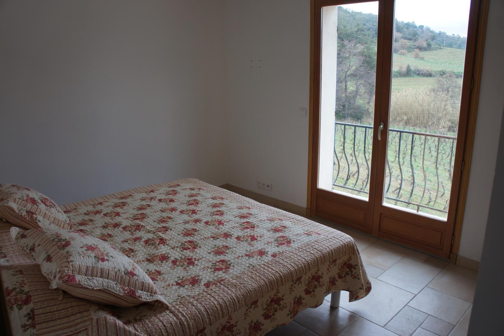 A bedroom with a bed, a window with a view of a green landscape, and a balcony with a metal railing.