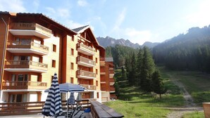 Un edificio in legno a più piani con balconi, un pontile in legno con tavolo e sedie, e vista su un paesaggio montuoso.