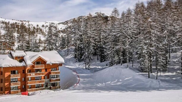 Un lodge in legno a più piani con balconi, circondato da alberi innevati e una pista da sci.