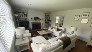 A living room with a fireplace, white furniture, and a bookshelf.