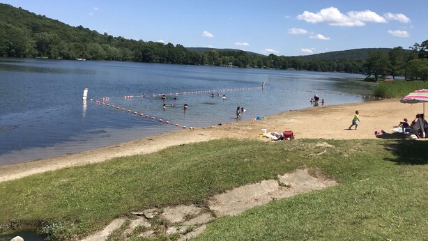 A lake with a grassy shore, a sandy beach, and a few people and boats.