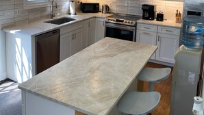 A modern kitchen with white cabinets, a central island, stainless steel appliances, and a water dispenser.