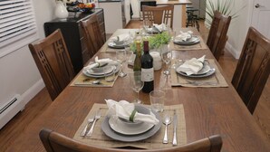 A dining table set for six with plates, glasses, and a bottle of wine.
