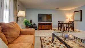 A living room with a sofa, TV, dining table, chairs, and a patterned rug.