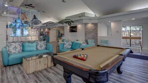 A modern living room with a pool table, a sofa set, and ceiling fans.