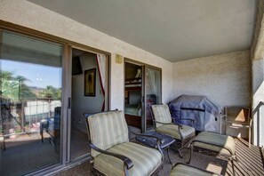 Un balcon avec des portes-fenêtres coulissantes, un canapé, un fauteuil et un téléviseur.