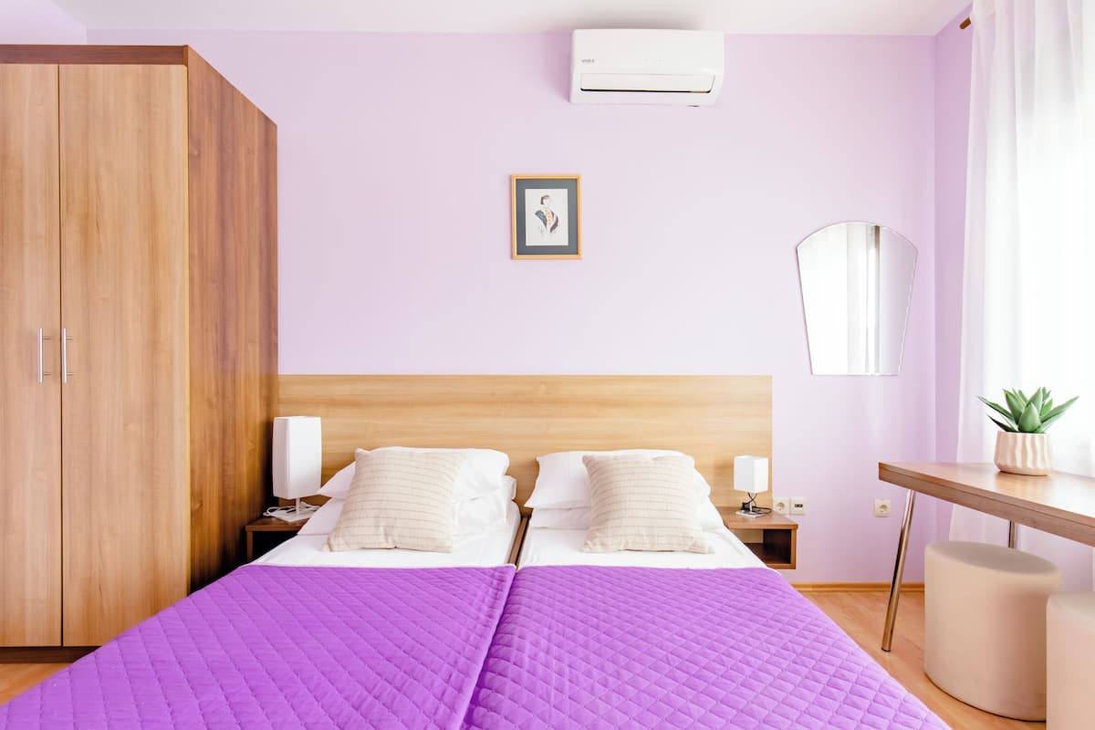 Een slaapkamer met een houten garderobe, een bed met een paars quilt, een nachtkastje met een lamp en een kleine plant op een bureau.