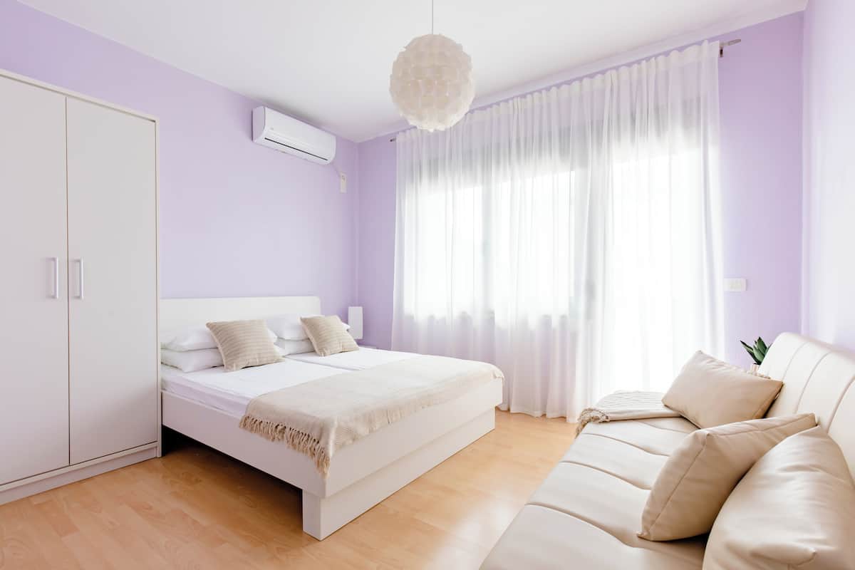 Een slaapkamer met een bed, een slaapbank, een kledingkast en een raam met gordijnen.