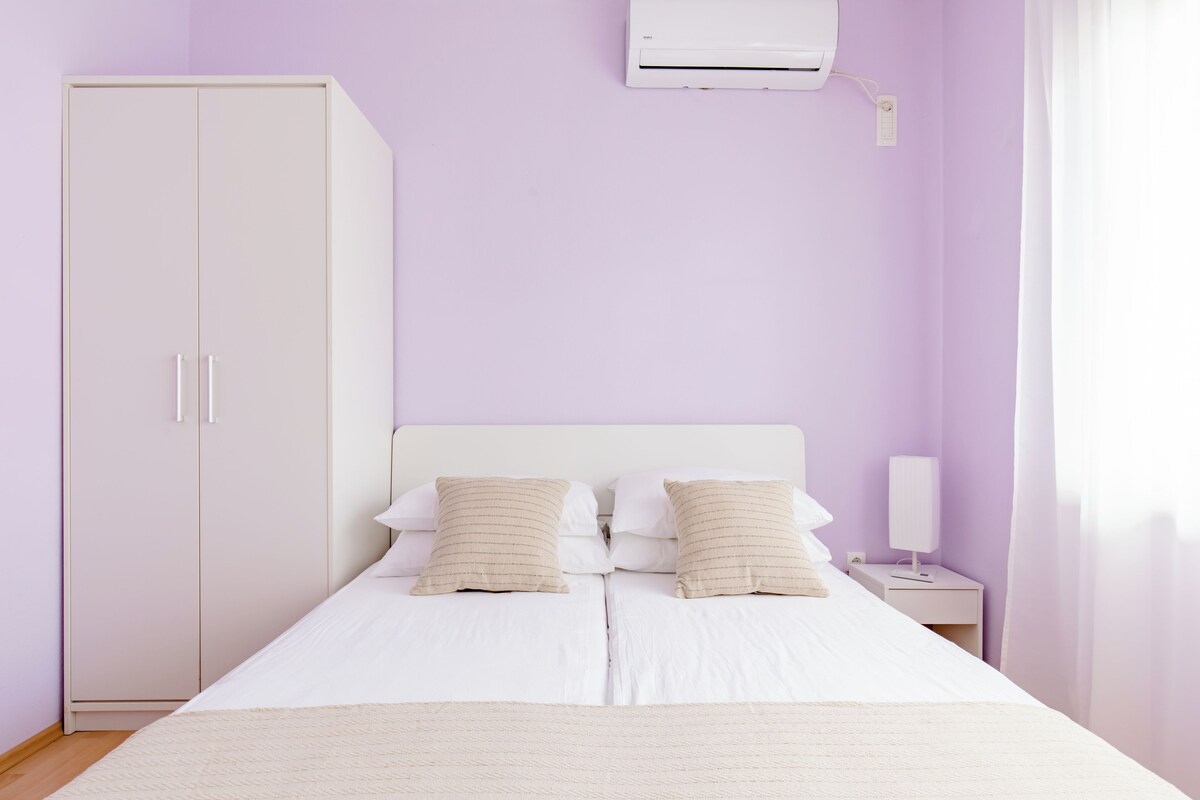 A bedroom with a bed, two bedside tables, a wardrobe, and an air conditioning unit.