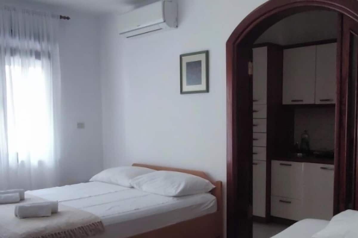 Hotelkamer met twee bedden, een houten vloer, een airconditioningapparaat, een raam met gordijnen en een garderobe.
