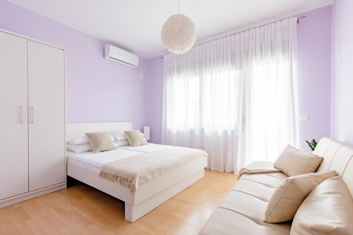 A bedroom with a bed, a sofa, a wardrobe, and a window with curtains.