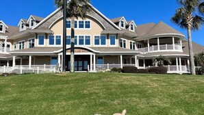 A large, two-story house with a curved roof, a white fence, and a lawn. - Popular Spinnaker Beach House! Close to Beach! Amenity access included! (Seabrook Island)