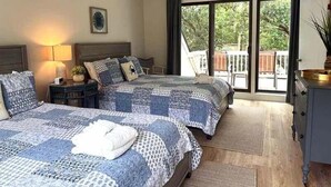 A bedroom with two beds, a nightstand, a lamp, a dresser, and a sliding glass door leading to an outdoor area. - Popular Spinnaker Beach House! Close to Beach! Amenity access included! (Seabrook Island)