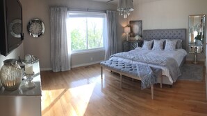 A bedroom with a large bed, a bedside table, a mirror, and a window with curtains.