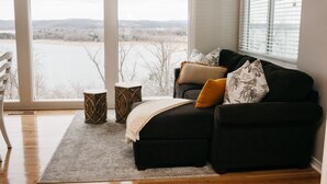 A living room with a black sofa, a white chair, and a view of a lake through large windows.