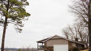 A two-story house with a stone foundation and a garage, located near a body of water.
