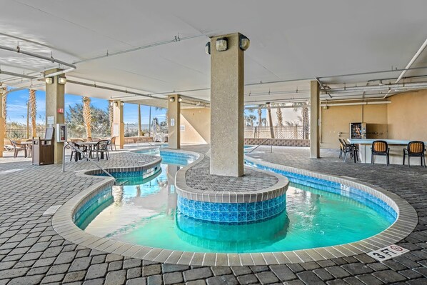 A pool area with a central hot tub, seating around the pool, and a covered section with tables and chairs.