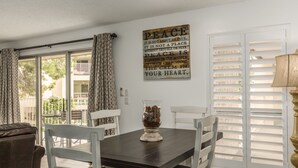 A dining area with a dark wooden table, white chairs, and a decorative vase. A wall-mounted sign with a peace quote is visible.
