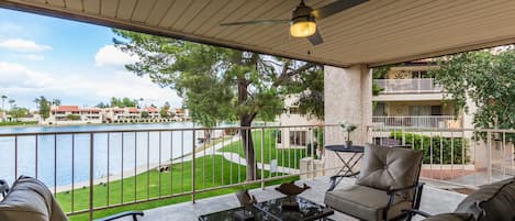 A covered outdoor patio with a view of a lake, a pool, and a lawn.