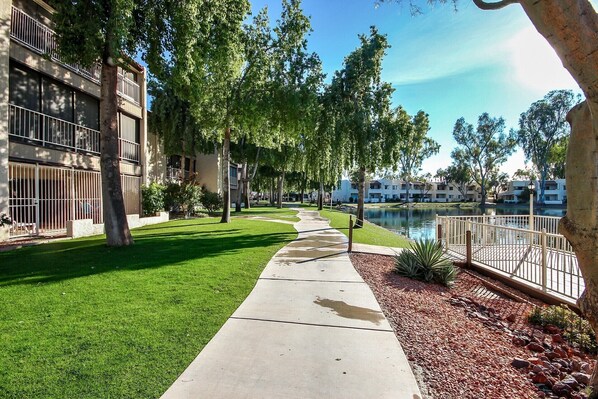 A pathway leading to a building with a water feature and a view of other buildings in the background.