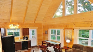 A cozy cabin interior with a wooden interior, a dining area, a kitchen, and large windows offering views of the outdoors.