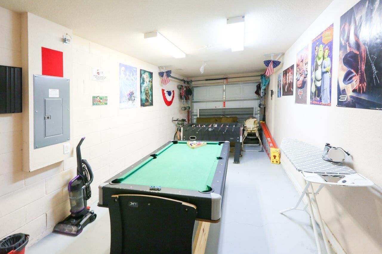 Uma mesa de bilhar em um espaço com porta de garagem, aspirador de pó e uma mesa com tábua de passar.