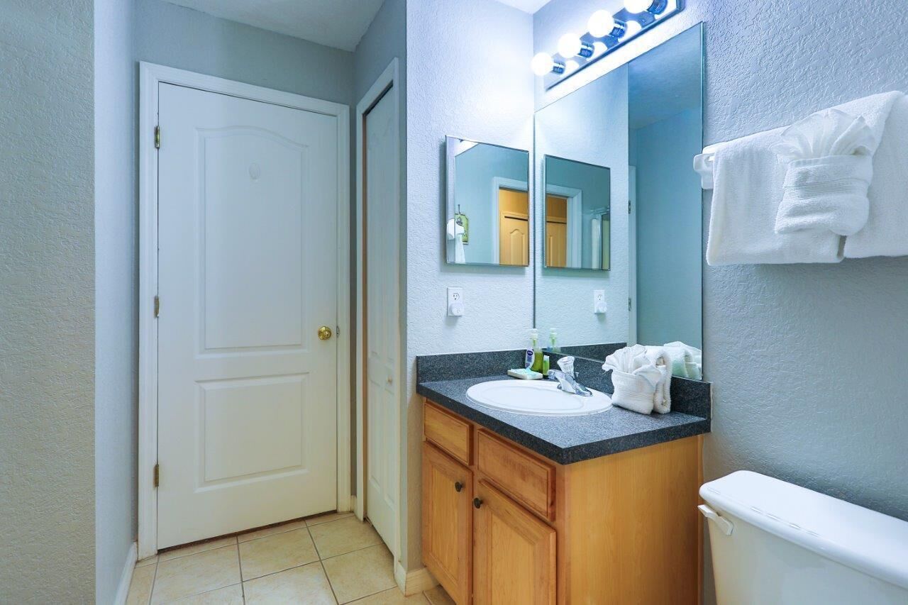 Un baño con una puerta blanca, un lavabo con un espejo encima y una toalla colgada en la pared.