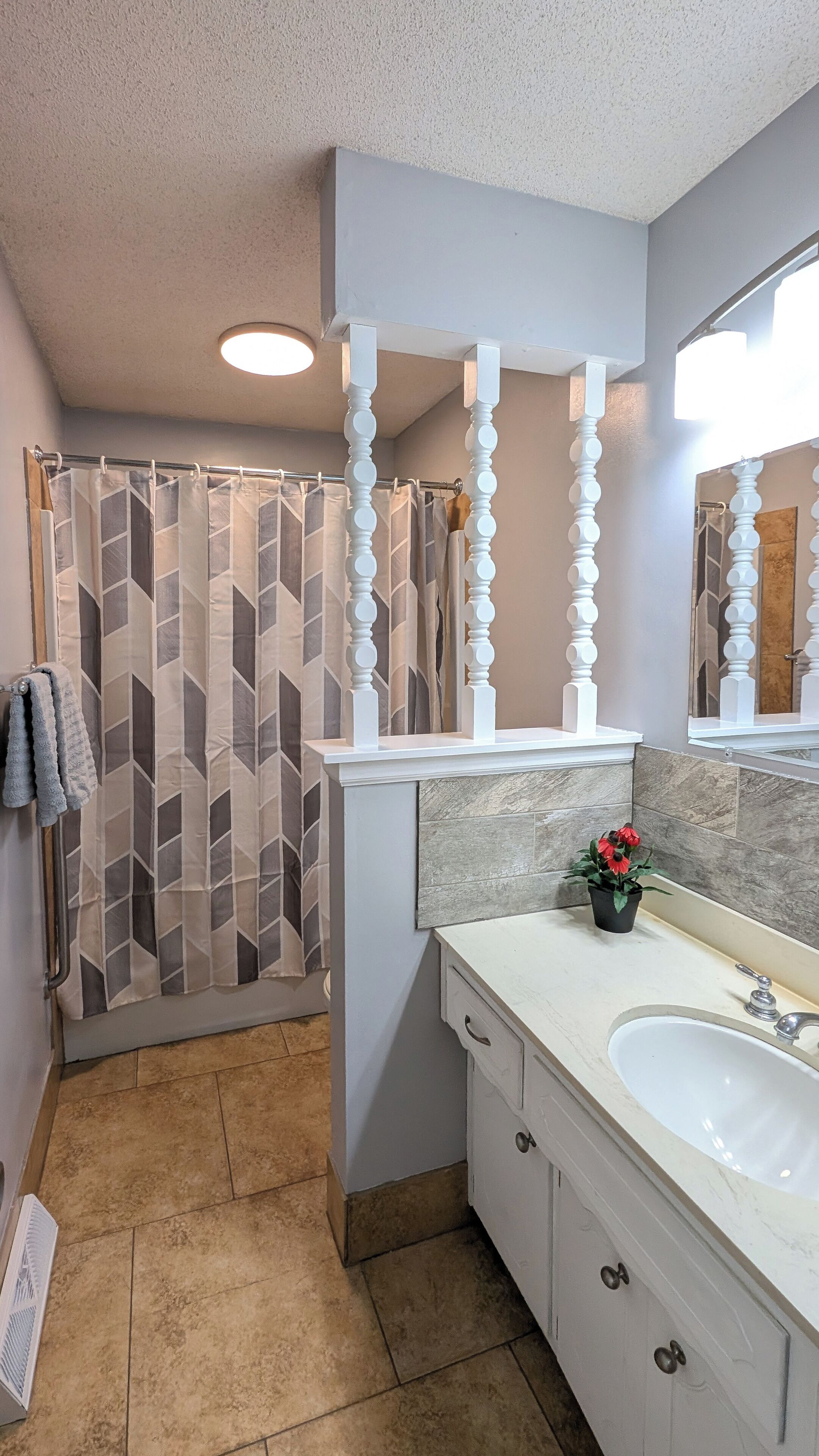 A bathroom with a shower curtain, a sink, a mirror, and a potted plant.