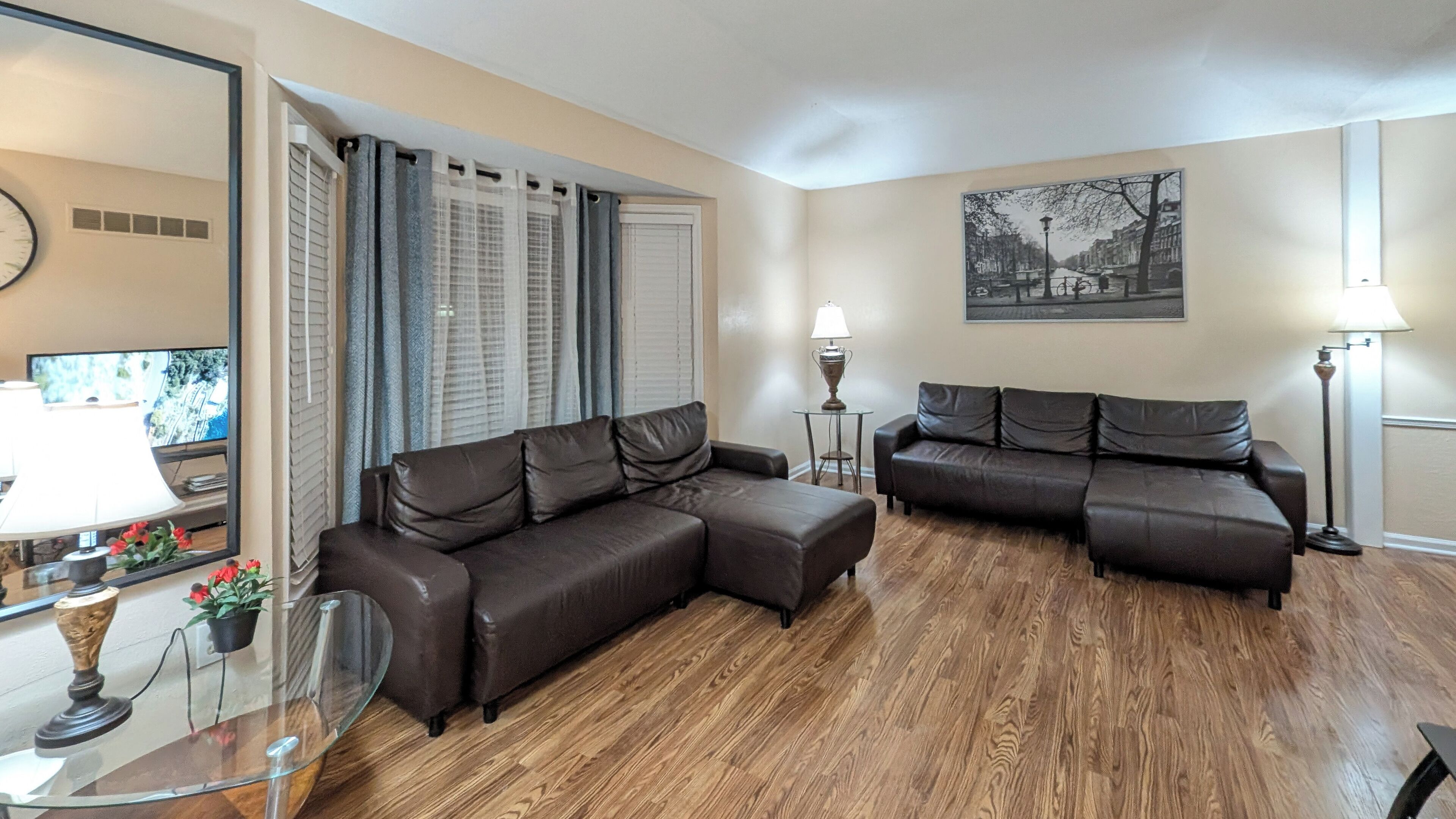 Ein Wohnzimmer mit zwei braunen Ledersofas, einem Glastisch, einer Lampe und einem gerahmten Stadtbild an der Wand.