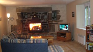 A living room with a stone fireplace, a television, a sofa, and a bookshelf. - Spacious farmhouse ,wheelchair accessible , close to stunning beaches . (Landudec)