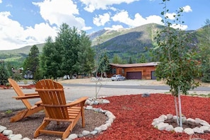 A wooden chair and table in a landscaped area with a mountain backdrop.