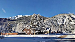 A house with a snow-covered landscape and mountains in the background.