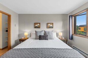 Een slaapkamer met een bed, twee nachtkastjes, twee wandlampen, twee ingelijste foto's en een raam met uitzicht.