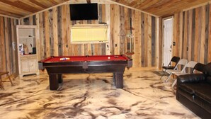 Una sala con piscina, mesa de billar, televisor montado en la pared y techo de madera.