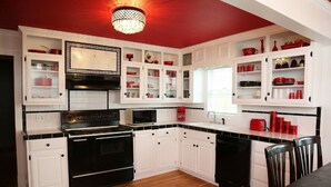 Una cocina con armarios blancos, electrodomésticos negros y detalles en rojo.