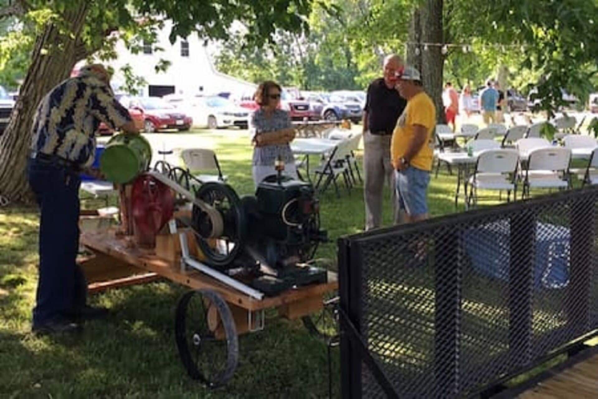 A vintage car on display at an outdoor event, with a grassy area and parked cars in the background.
