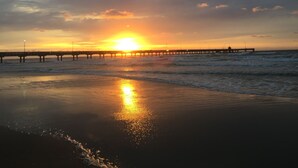 Uma praia com um píer se estendendo para o oceano durante o pôr do sol.